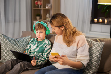 family, technology and people concept - happy mother and little son sitting on sofa with tablet pc...