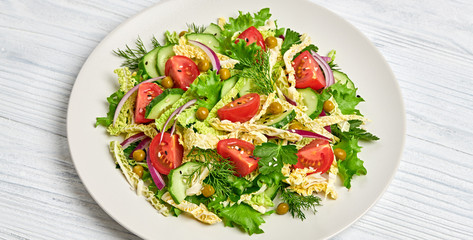 Fresh salad with cherry tomatoes, savoy cabbage, cucumeber on dish. Healthy summer salad vegetarian meal concept. Tasty mixed leaves, tomatoes and mix vegetable salad on white wood