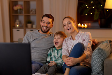 family, leisure and people concept - happy smiling father, mother and little son with remote control watching tv at home at night