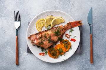 Baked sea bass with tomato pepper lemon and herbs in a ceramic plate on a gray concrete background. Perch fish cooked in the oven. Copy space Top view