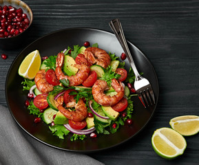 Shrimps salad, avocado, lettuce, cherry tomatoes. Home made vegetarian shrimp salad. Seafood concept. Tasty veg mixed leaves, grilled prawn shrimps in plate on black wood background.