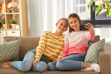 Obraz premium people, technology and friendship concept - happy teenage girls taking selfie with smartphone sitting on sofa at home