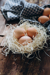 Brown chicken eggs in a white nest on an old wooden rustic background. The blue fabric lies
