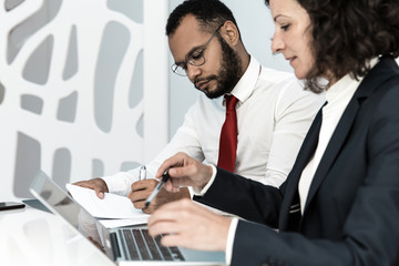 Two office employees studying during training. Business man and woman sitting at conference table, using laptop, writing in papers. Business training concept