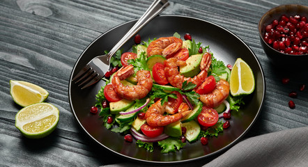Shrimps salad, avocado, lettuce, cherry tomatoes. Home made vegetarian shrimp salad. Seafood concept. Tasty veg mixed leaves, grilled prawn shrimps in plate on black wood background.