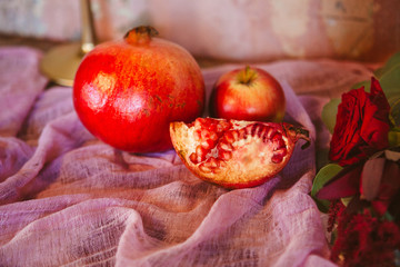 Whole and broken into pieces pomegranates are laid out on a pink fabric served with an apple on a rustic table