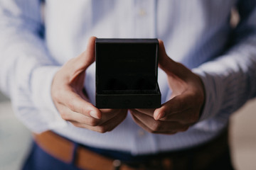 Closeup of gift on male hands. Man in blue shirt. Unrecognizable man holding opening black present box. Special day and festive event concept. 2 man's Hands with copy space.