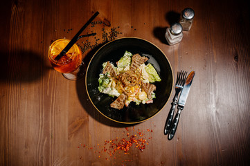 Caesar salad on black plate on wooden table.Top view