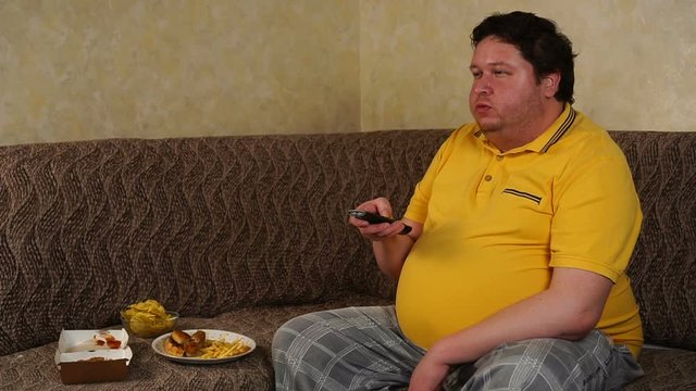 Fat man sitting at home watching tv and eating fast food