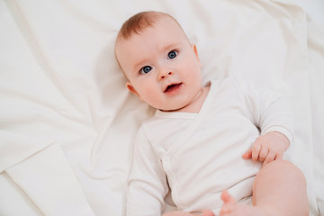 baby in white clothes lying on his back on the bed