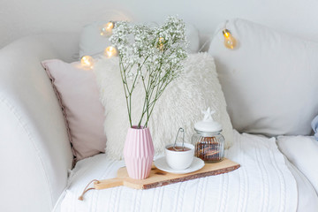 Spring home cozy interior. A bouquet of flowers in a vase, a cup of tea, decor on the sofa.