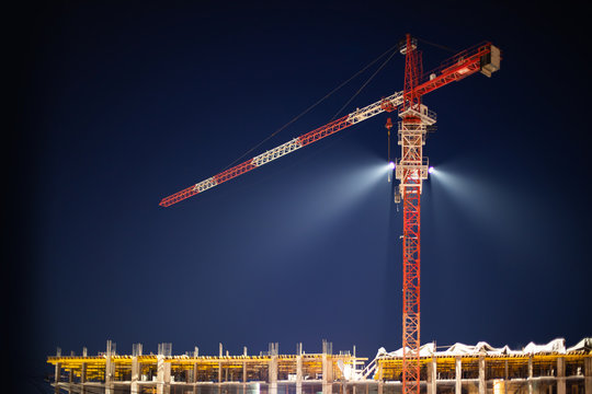 Construction Crane In Night Illumination, Construction Of A Multi-storey Modern Residential Building. Night Construction Site, Twilight Spotlight