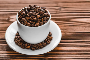 full white cup with coffee beans with plate on brown wooden background