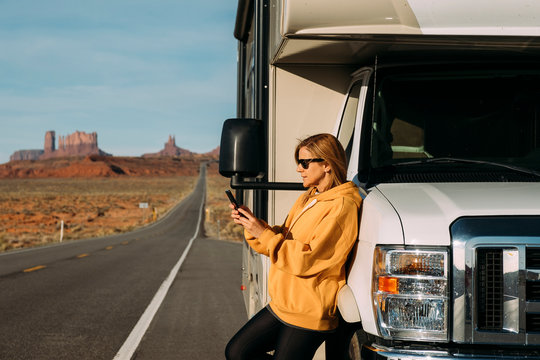 A woman travels by motorhome through Monument Valley in the USA desert and checks her mobile phone parked on the side of the road