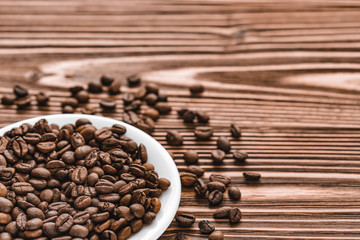full white plate of coffee beans on brown wooden background. scattered grains around the saucer