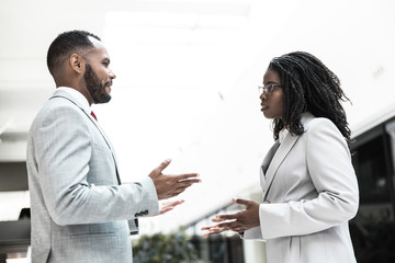 Serious confident business partners discussing project in office hall. Business man and woman standing and talking to each other. Business meeting or negotiation concept