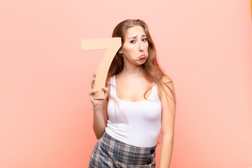 yound blonde woman sad, depressed, unhappy, holding a number 7.