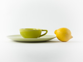 Image of a cup of tea and lemon in pastel green and yellow colors on a white background. Modern forn and minimal food idea, healthy lifestyle concept.