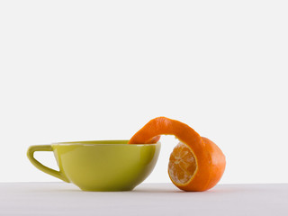 Fresh peeled orange and  cup of tea in pastel green and yellow color on a white background. Drinks with fruit, minimal food idea, healthy lifestyle concept.