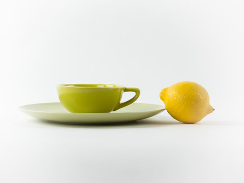 Image of a cup of tea and lemon in pastel green and yellow colors on a white background. Modern forn and minimal food idea, healthy lifestyle concept.