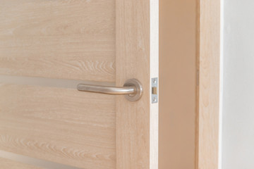 Open bright wooden door with a lock and a metal handle in a hotel or apartment room