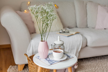 Spring home cozy interior. A bouquet of flowers in a vase, a cup of tea, decor on a coffee table.