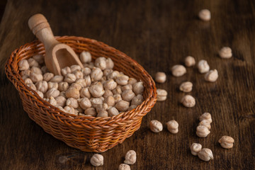 Close-up of basket with raw chickpeas on dark wooden table, dark light in horizontal