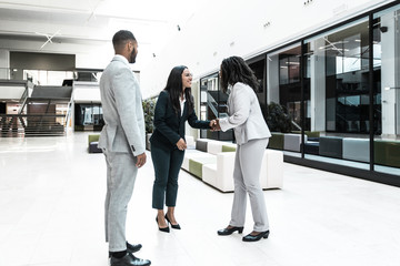 Fototapeta premium Happy successful businesswoman welcoming partners in hallway. Business man and women standing in office hall, shaking hands with each other, talking and smiling. Business relationship concept