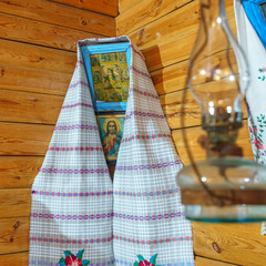 An icon depicting the Virgin Mary of Our Lady, decorated with a towel with a bedspread in a wooden house in the red corner. In the foreground an oil lamp in defocus. Christmas and Easter concept.
