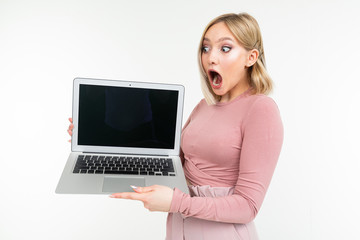 surprised blonde girl in pink clothes holds a laptop with the display forward with an empty blank on a white studio background