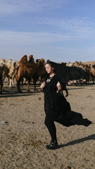 beautiful woman national eastern clothes black color,veil,hijab,abaya ornament her head,portrait steppes camels,strong wind,desert,wildlife,well,decoration,caucasian,slow ,sun
