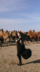 beautiful woman national eastern clothes black color,veil,hijab,abaya ornament her head,portrait steppes camels,strong wind,desert,wildlife,well,decoration,caucasian,slow ,sun