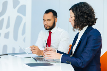 Serious business colleagues with computer and documents discussing ongoing project. Business man and woman with laptop and papers sitting at conference table and talking. Colleagues concept