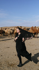 beautiful woman national eastern clothes black color,veil,hijab,abaya ornament her head,portrait steppes camels,strong wind,desert,wildlife,well,decoration,caucasian,slow ,sun