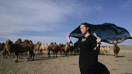 beautiful woman national eastern clothes black color,veil,hijab,abaya ornament her head,portrait steppes camels,strong wind,desert,wildlife,well,decoration,caucasian,slow ,sun
