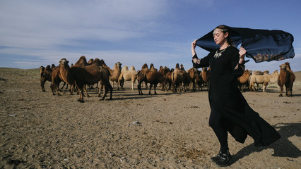beautiful woman national eastern clothes black color,veil,hijab,abaya ornament her head,portrait steppes camels,strong wind,desert,wildlife,well,decoration,caucasian,slow ,sun