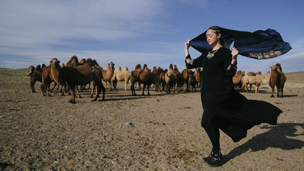beautiful woman national eastern clothes black color,veil,hijab,abaya ornament her head,portrait steppes camels,strong wind,desert,wildlife,well,decoration,caucasian,slow ,sun