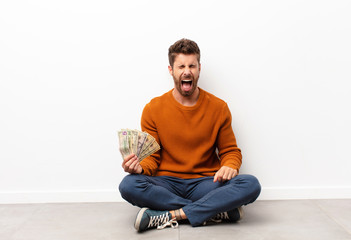 young handsome man shouting aggressively, looking very angry, frustrated, outraged or annoyed,...