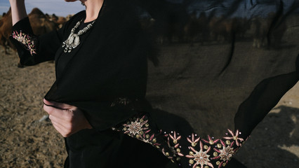 beautiful woman national eastern clothes black color,veil,hijab,abaya ornament her head,portrait steppes camels,strong wind,desert,wildlife,well,decoration,caucasian,slow ,sun