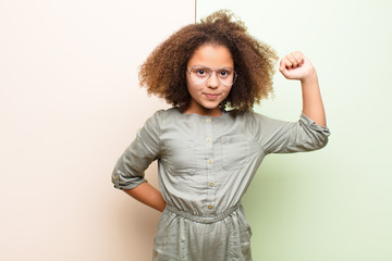 african american little girl feeling serious, strong and rebellious, raising fist up, protesting or...