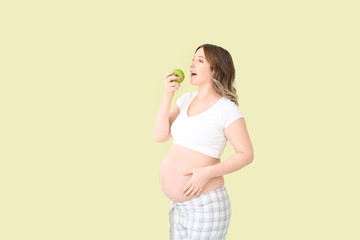 Beautiful pregnant woman with apple on color background