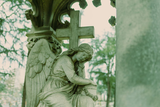 cementery angel looking down in green tone, gray stone cross, tombestone, sadness concept