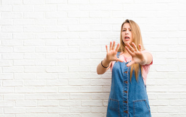 young blonde woman feeling terrified, backing off and screaming in horror and panic, reacting to a...
