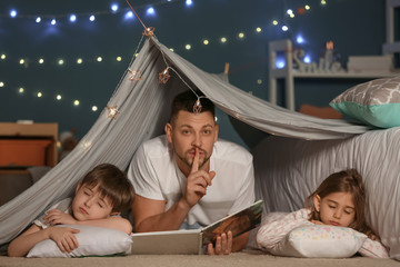 Father with book and his little sleeping children at home
