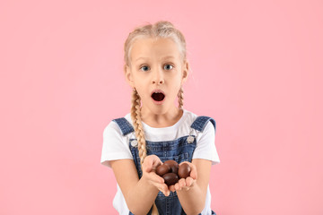 Surprised little girl with sweet chocolate eggs on color background