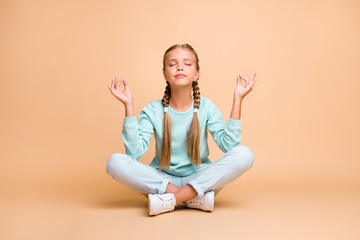 Full length photo of beautiful little lady sit floor legs crossed eyes closed fingers together lotus position meditating wear blue sweater jeans footwear isolated beige color background