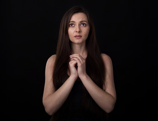 Faith in God. Young religious woman praying standing on a black background and looking up.