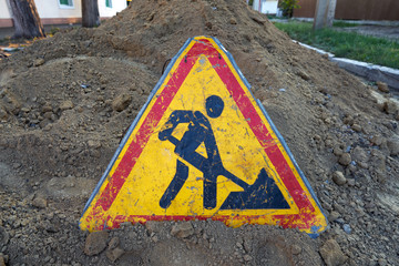 Road work sign placed on a pile of dug up land in the middle of a road being repaired