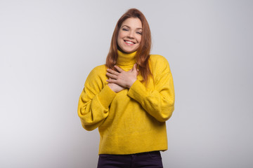 Cheerful young woman with hands on chest. Beautiful happy young woman holding hands near heart and smiling at camera. Love concept