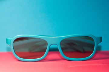 On bright pink background lie sunglasses in plastic blue frame with dark glasses. Summer. Accessories.